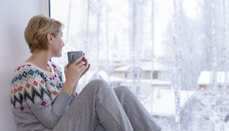 Decorative image: A woman sitting on the windowsill with a cup of tea in winter and looking out the panoramic window